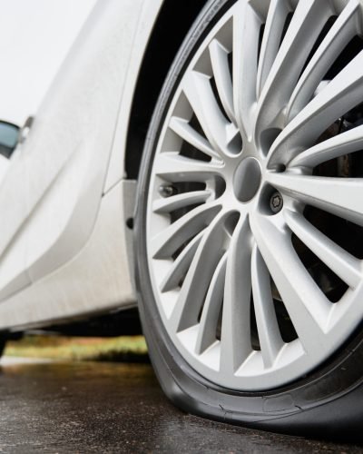 Close up view on stopped white car with punctured car tire on a road. Focus on a wheel.