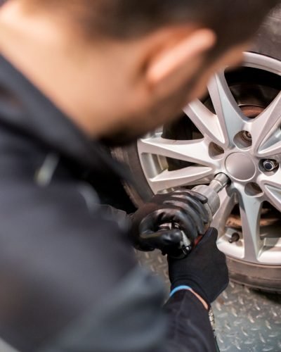 car service, repair, maintenance and people concept - auto mechanic man with electric screwdriver changing tire at workshop